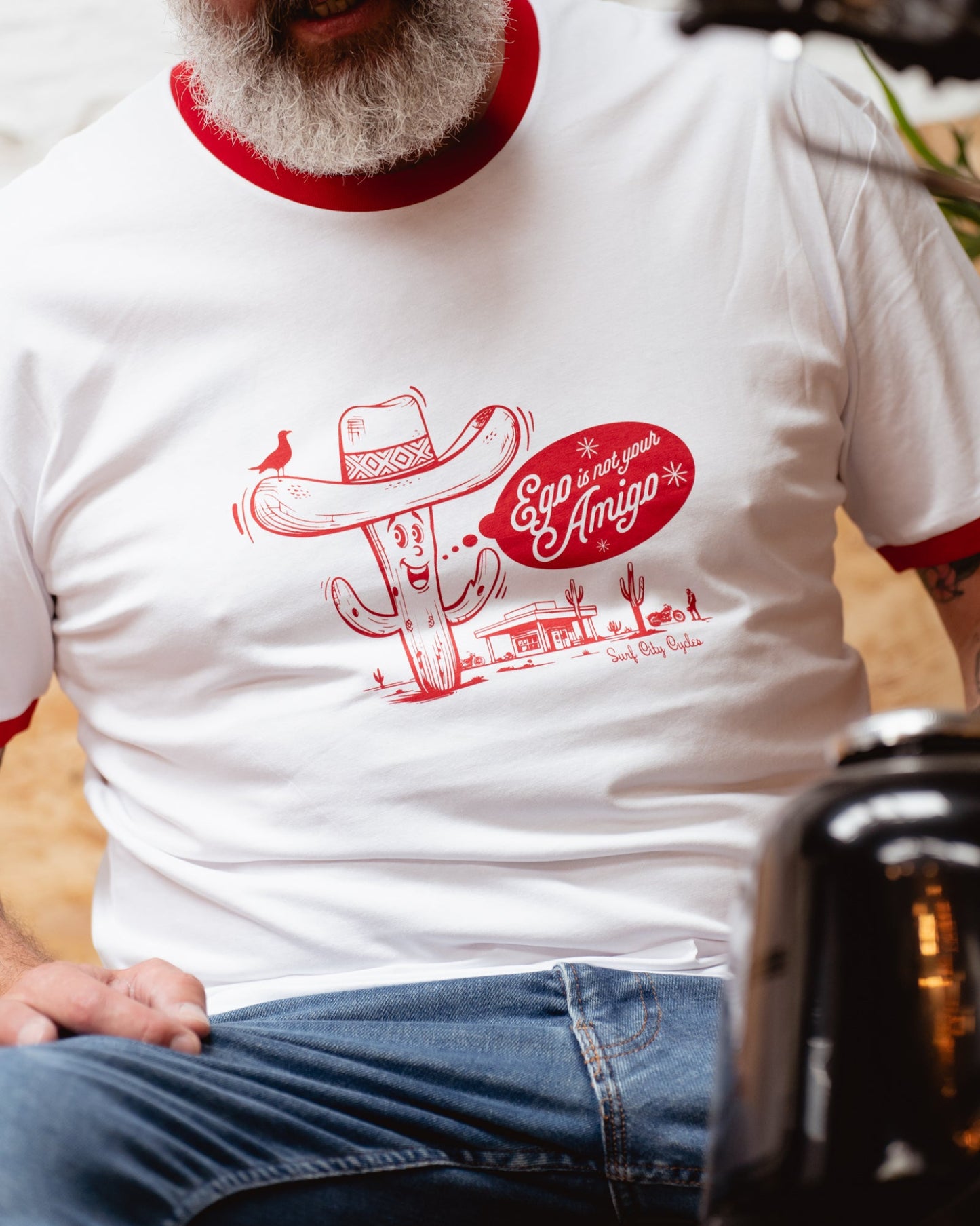 Close-up of “Ego is Not Your Amigo” red cactus graphic and red sleeve cuff on Surf City Cycles ringer tee