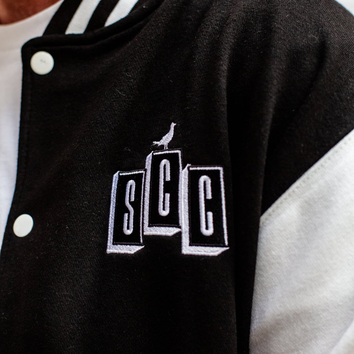 Tight detail shot of the white SCC block logo embroidery on the chest of the varsity jacket.