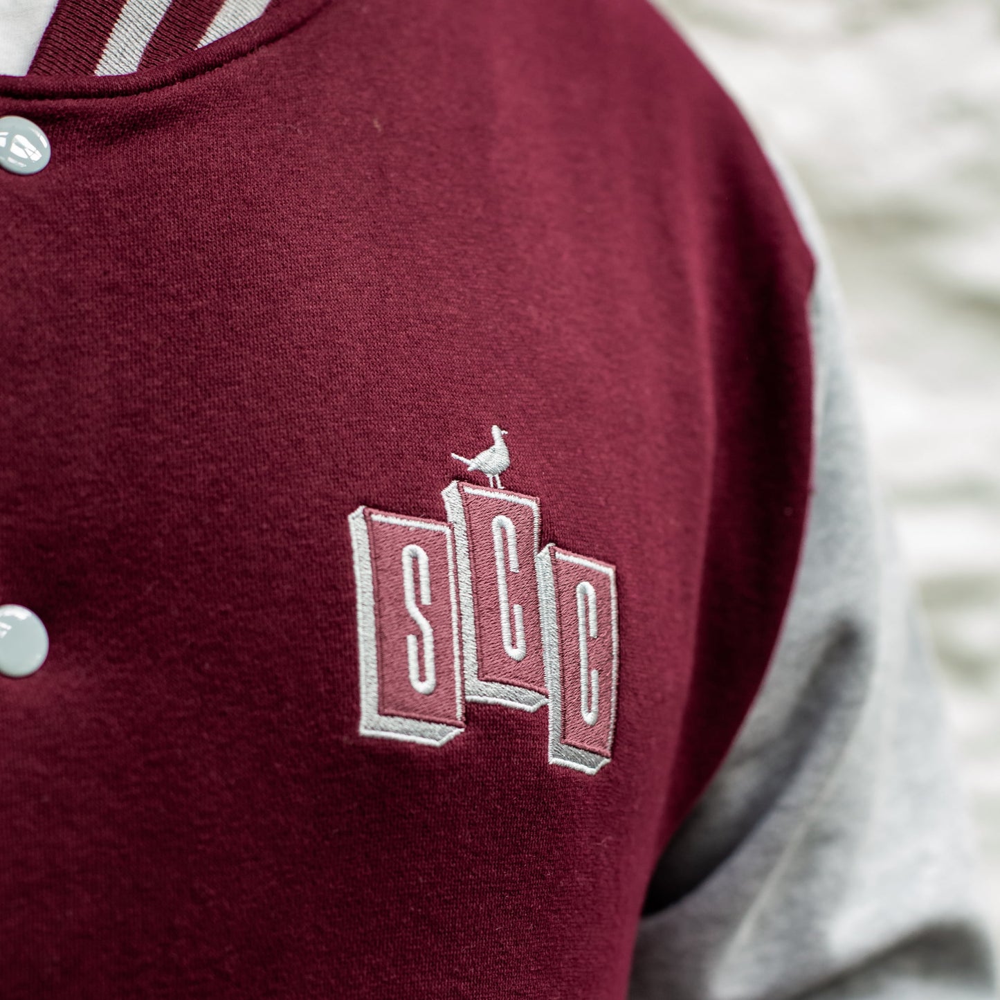Tight detail of the SCC block logo embroidery on the burgundy chest panel.