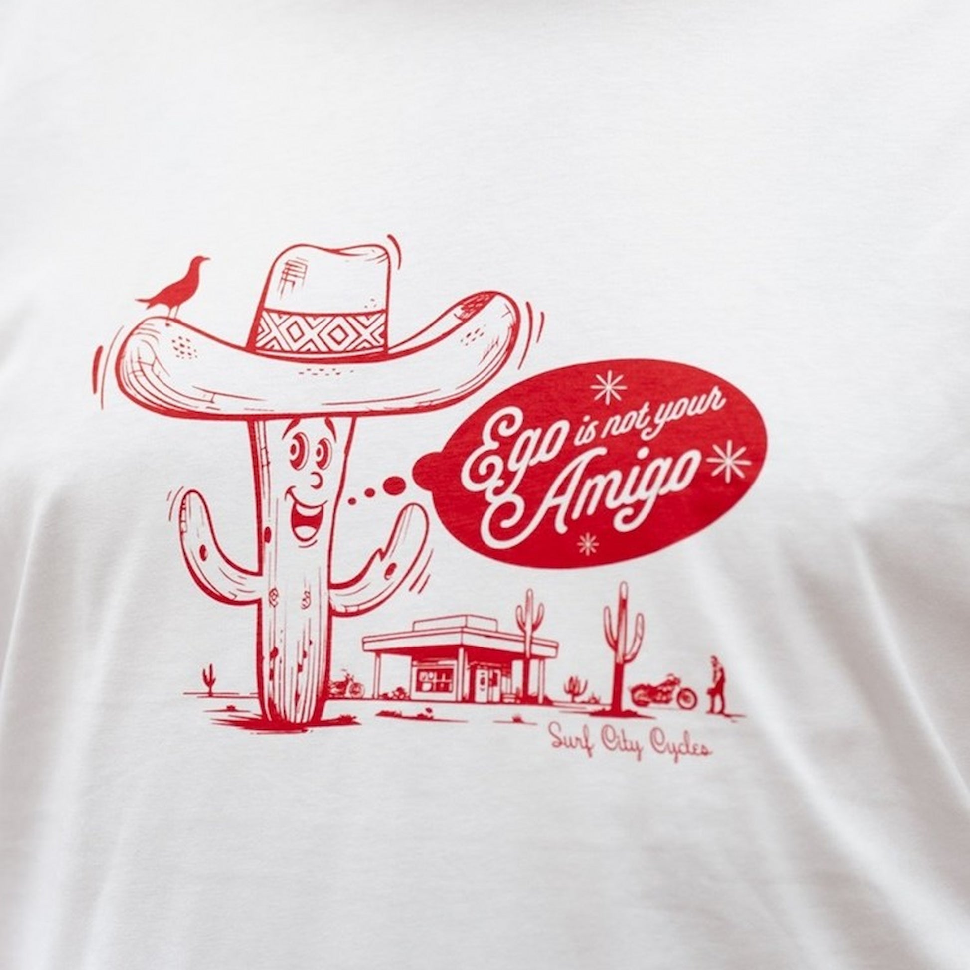Close-up of the red screen-printed cactus graphic and "Ego is not your Amigo" speech bubble on a white cotton tee.
