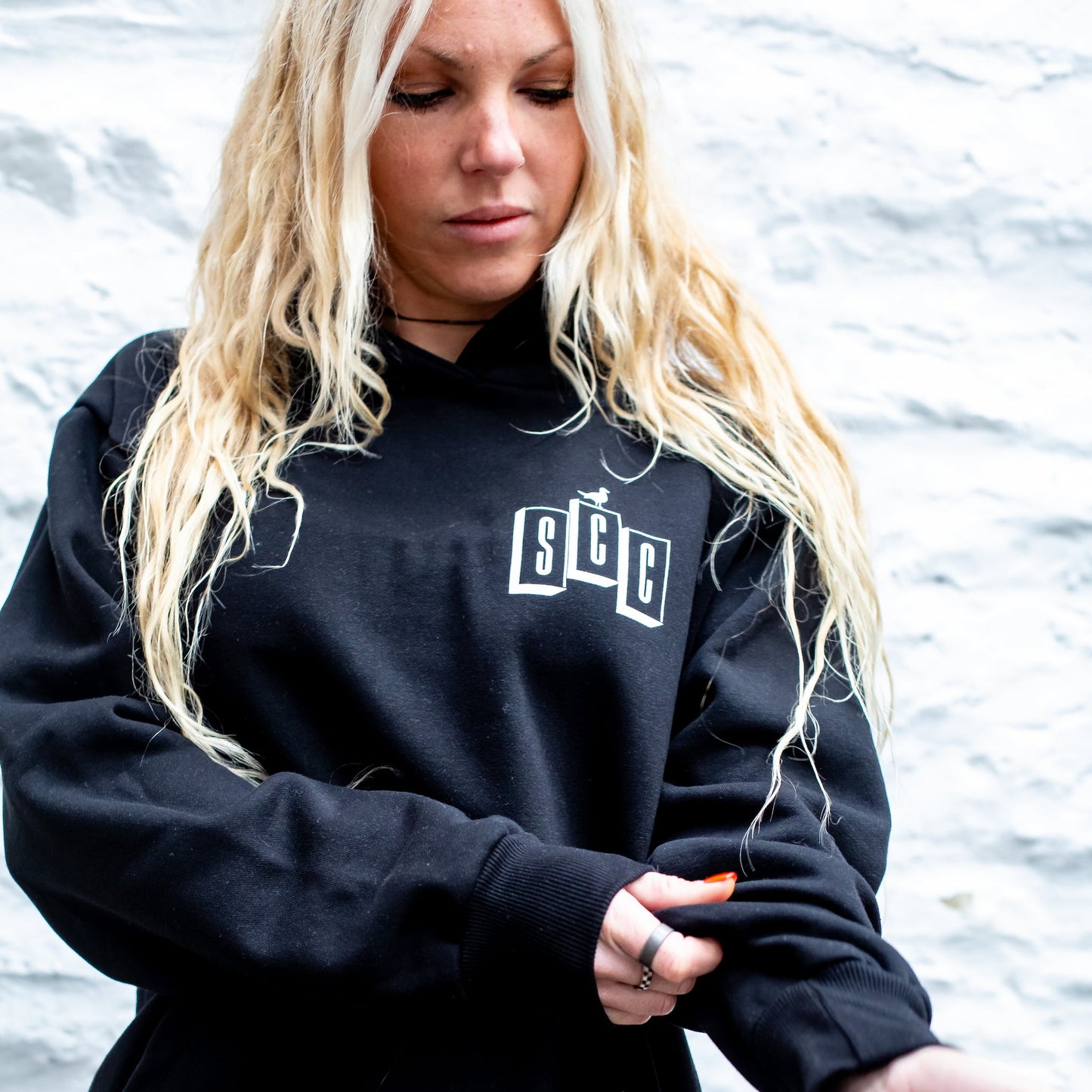 Person wearing a black hoodie with Surf City Cycles logo against a white stone wall background