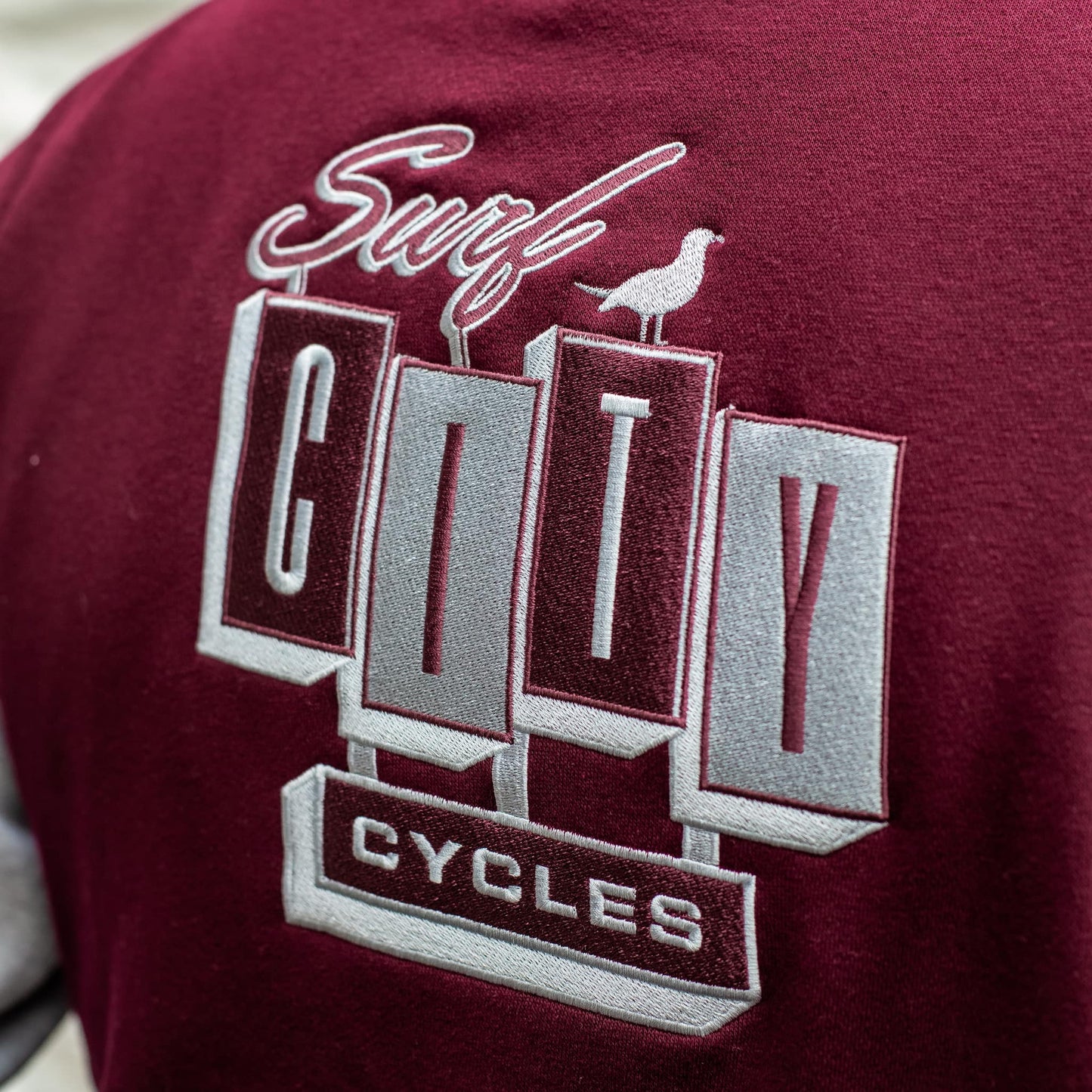 Close-up of the "Surf City Cycles" back embroidery on the burgundy varsity jacket.