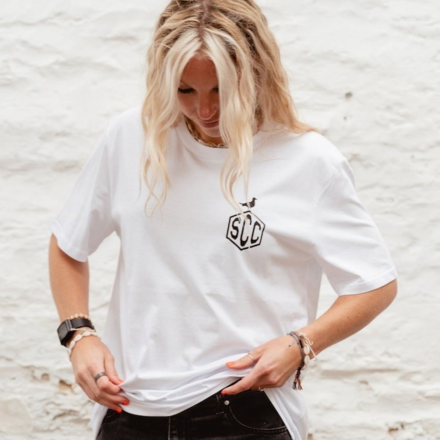 Female model wearing the white "Misadventure" crewneck organic cotton t-shirt against a white stone wall.