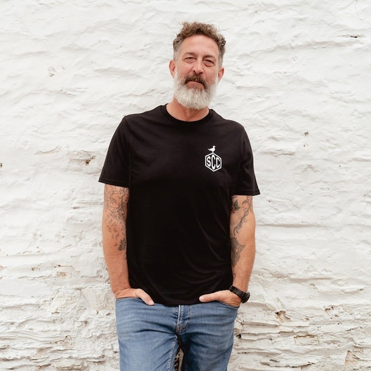 Bearded man wearing the black "Misadventure" t-shirt with a skeleton rider graphic against a white stone wall.