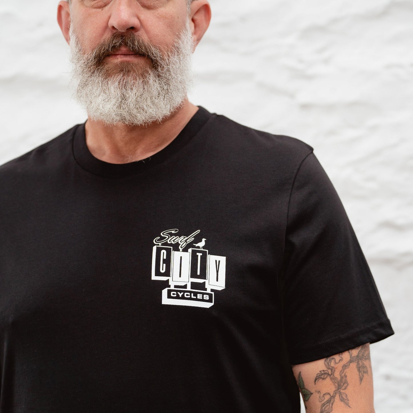 A detailed close-up of the white Surf City Cycles logo on the chest of a black organic cotton tee.