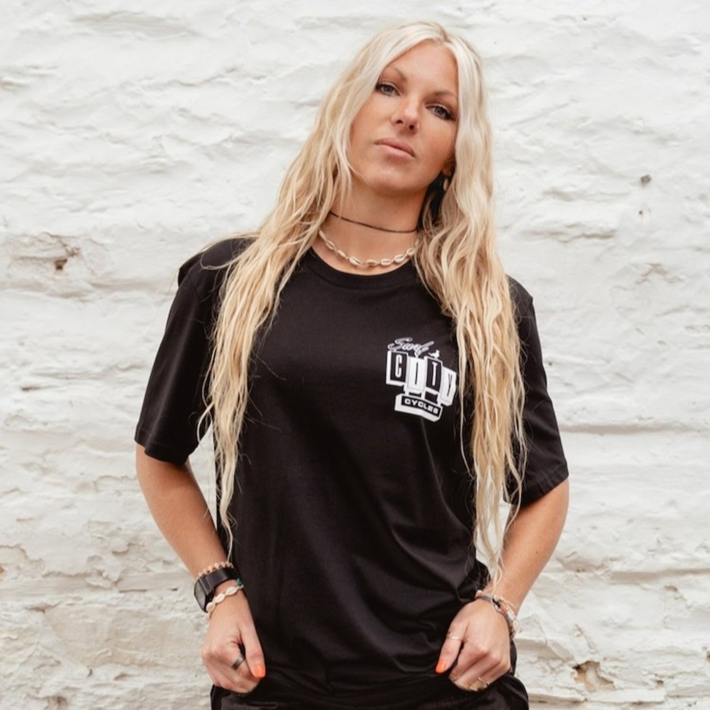 A female model wearing the OG Logo organic cotton tee in Black, featuring the high-contrast white Surf City Cycles block logo on the chest.