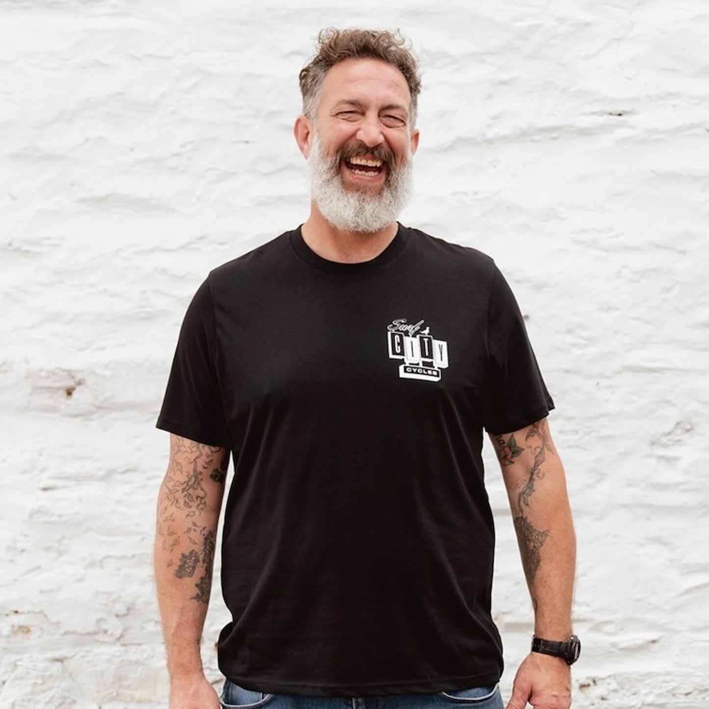 A male model with a grey beard laughing while wearing the Black OG Logo organic cotton tee, showcasing the white SCC block logo on the chest.