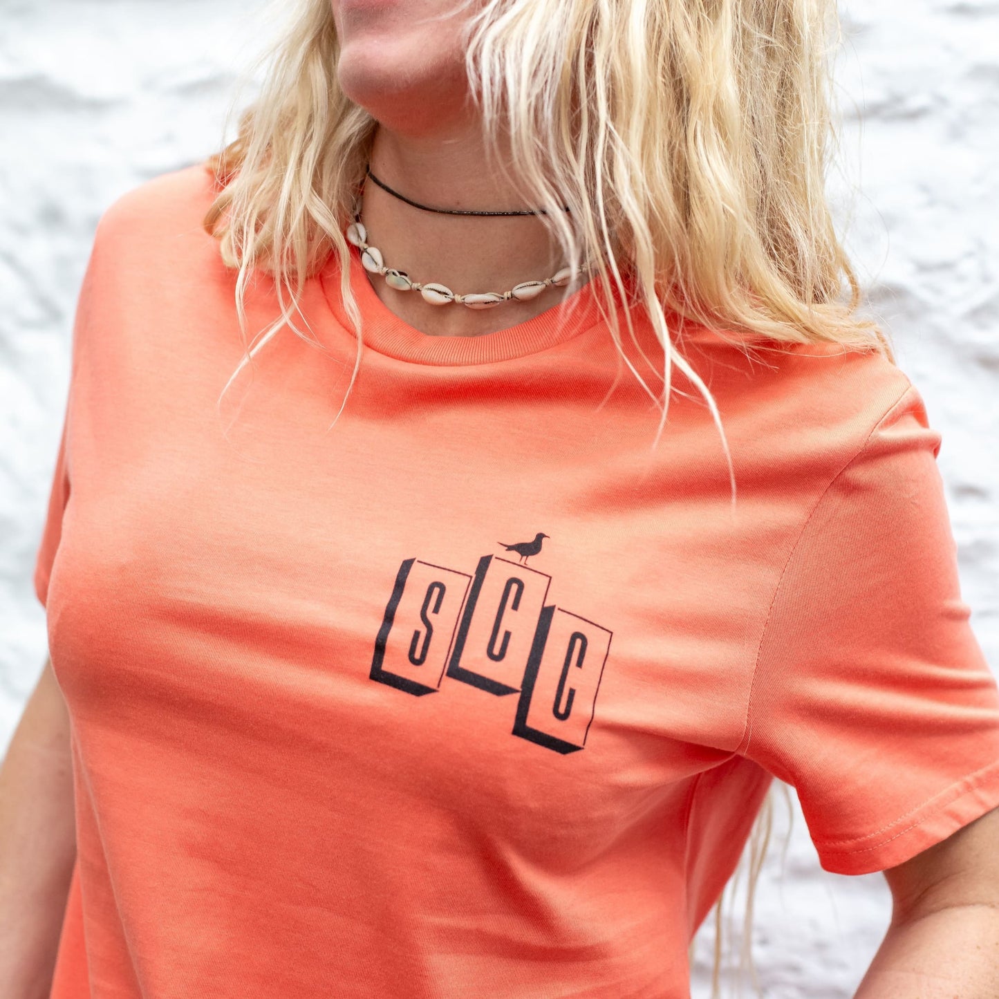 Close-up lifestyle shot of the OG Logo organic cotton tee in Fiesta, featuring the Surf City Cycles SCC block branding on the chest.