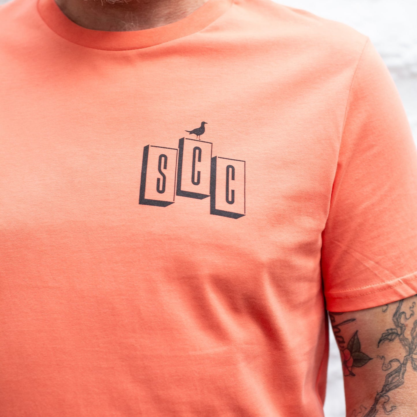 A detailed close-up of the SCC block logo and bird graphic on the chest of the Fiesta organic cotton tee.