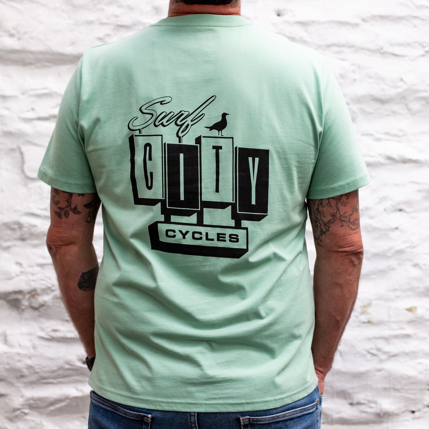 A detailed close-up of the back of the Seafoam OG Logo organic cotton tee, featuring the large Surf City Cycles block logo and bird graphic.