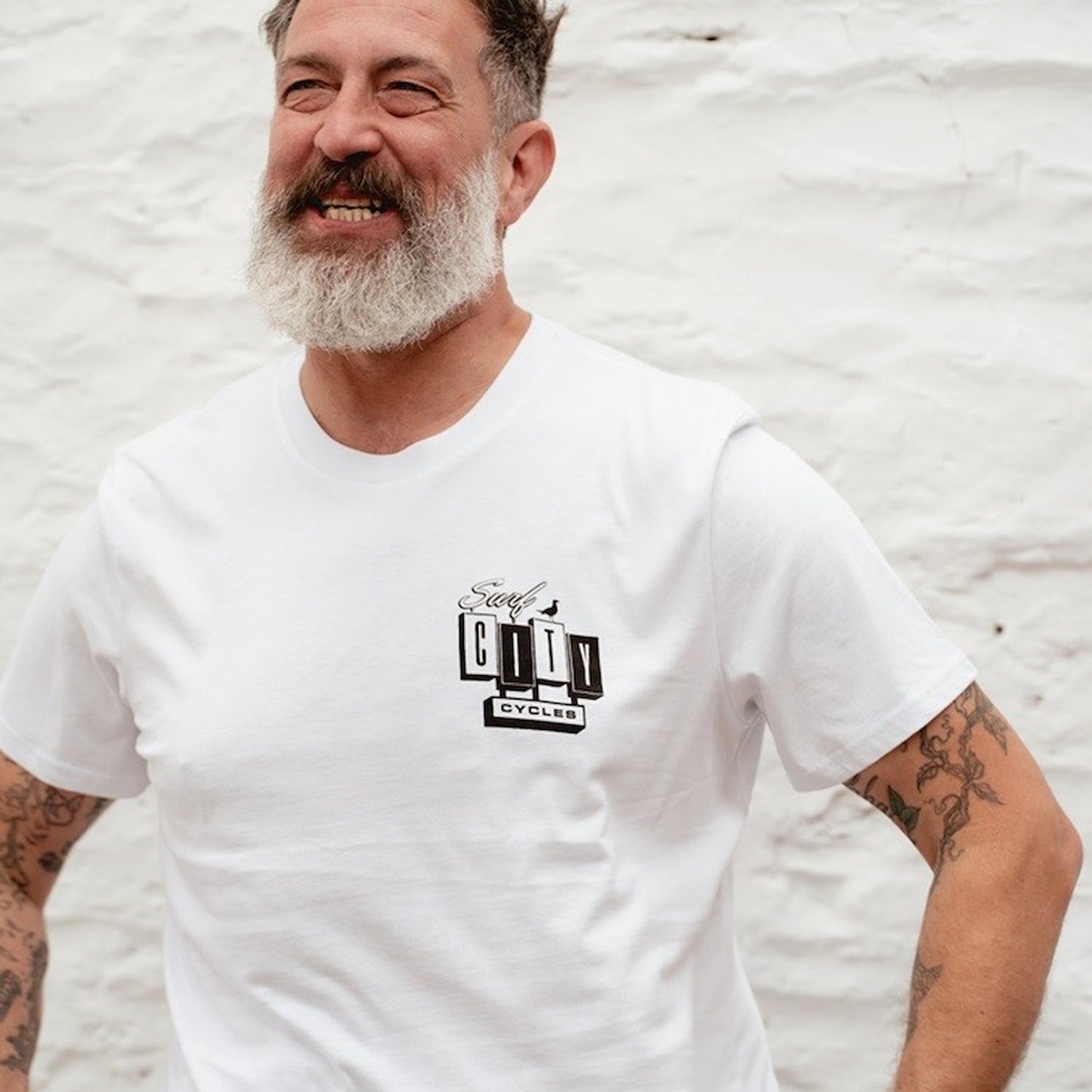 Portrait of a male model with a grey beard wearing the white OG Logo organic cotton tee, featuring the Surf City Cycles chest graphic.