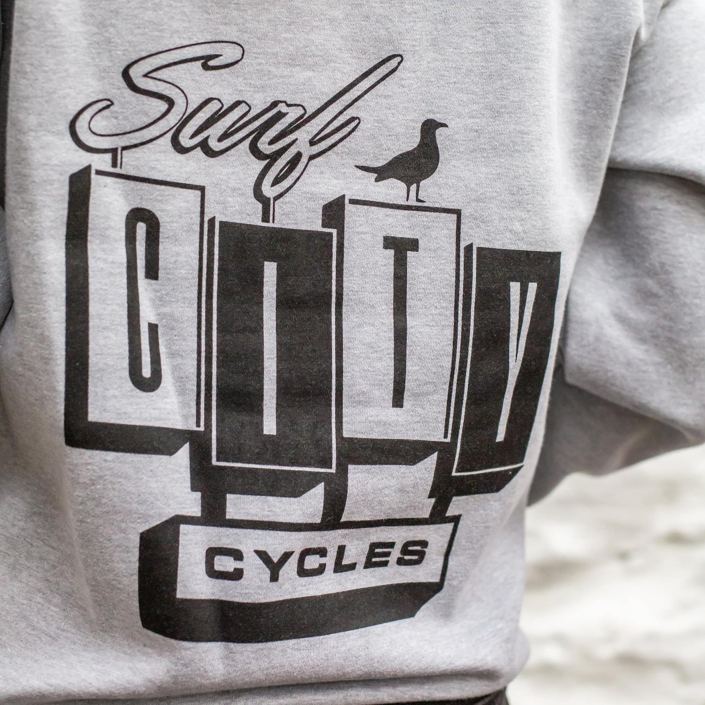 Rear view of a female model in the heather grey heavyweight hoodie, showing the relaxed fit and 3 panel hood structure.