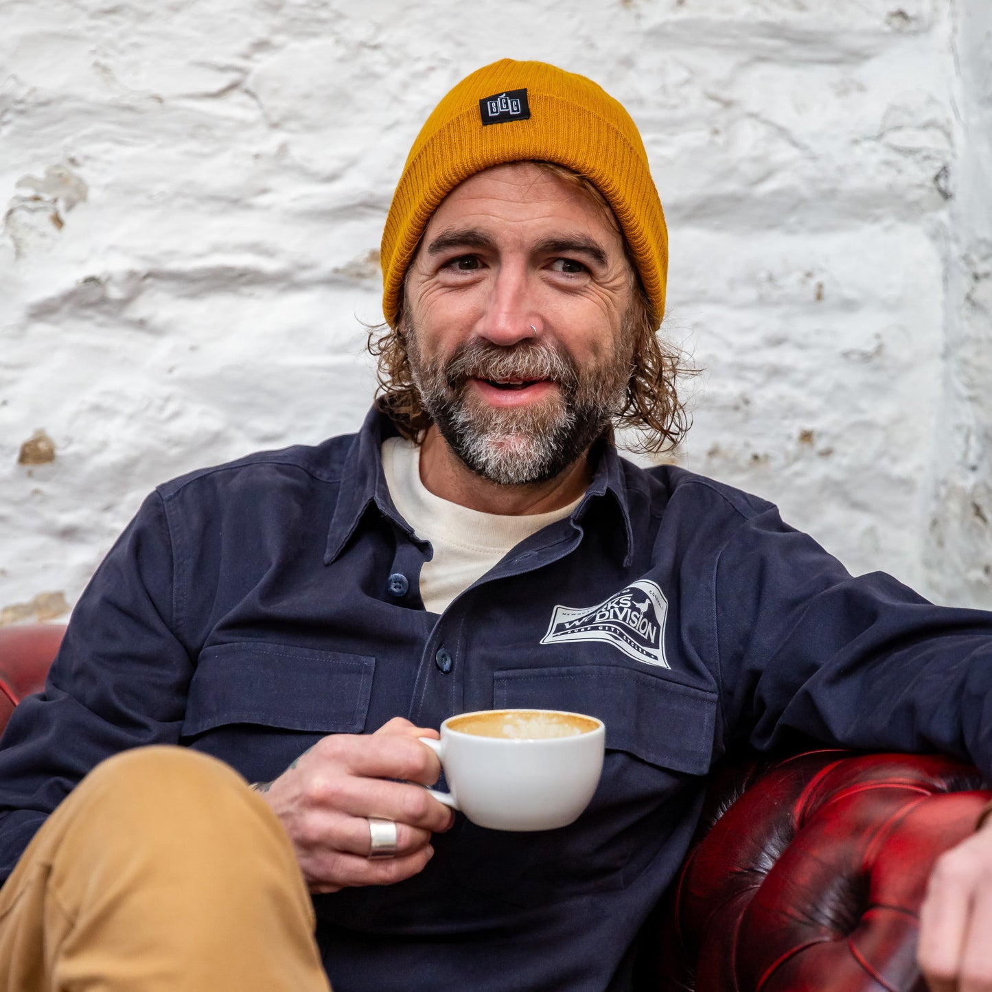 A male model wearing the Mustard Seafarer Organic Ribbed Beanie, styled with a Navy Works Division overshirt in a relaxed setting.