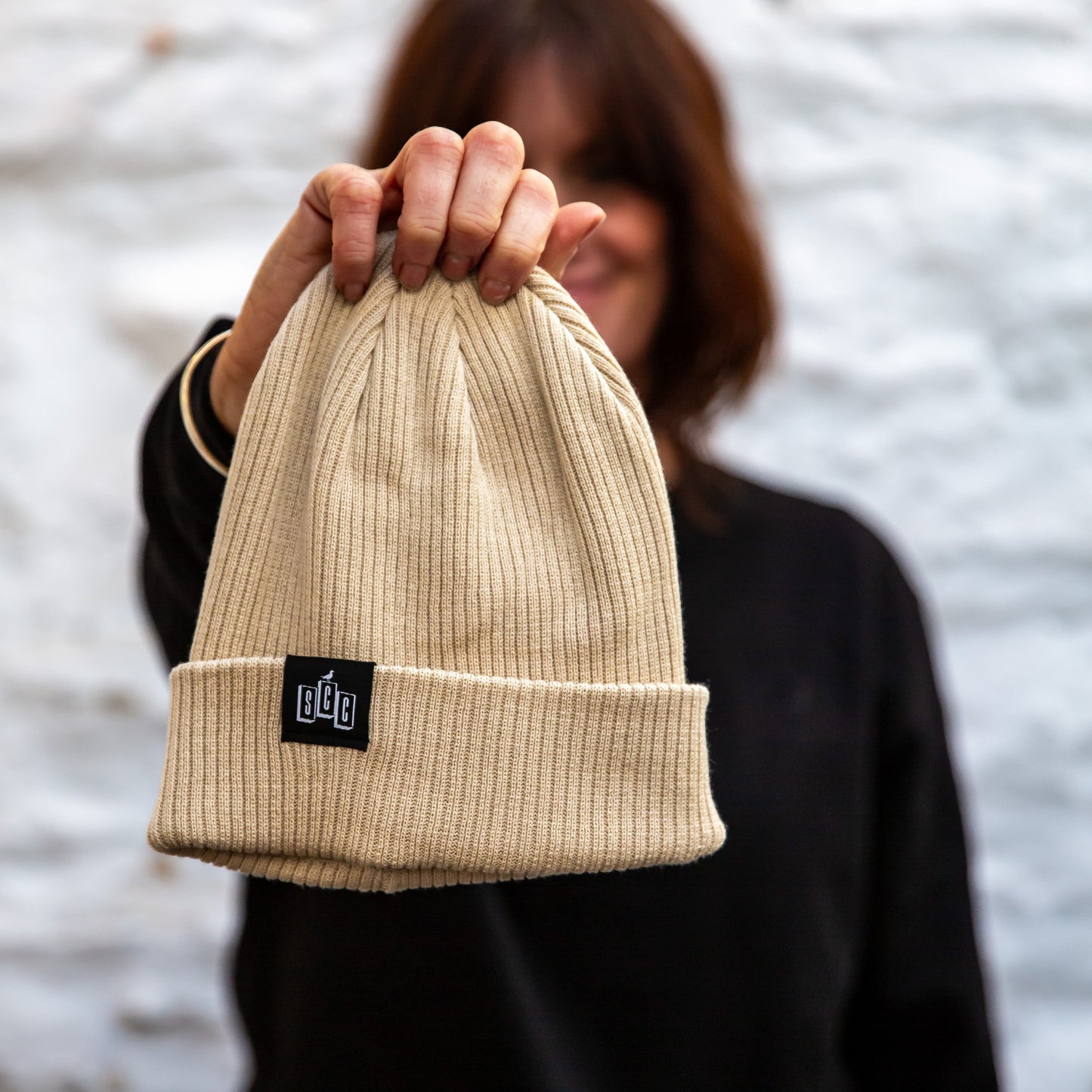 The Seafarer Organic Ribbed Beanie in Sand, a light neutral organic cotton rib-knit with the black SCC woven clip label