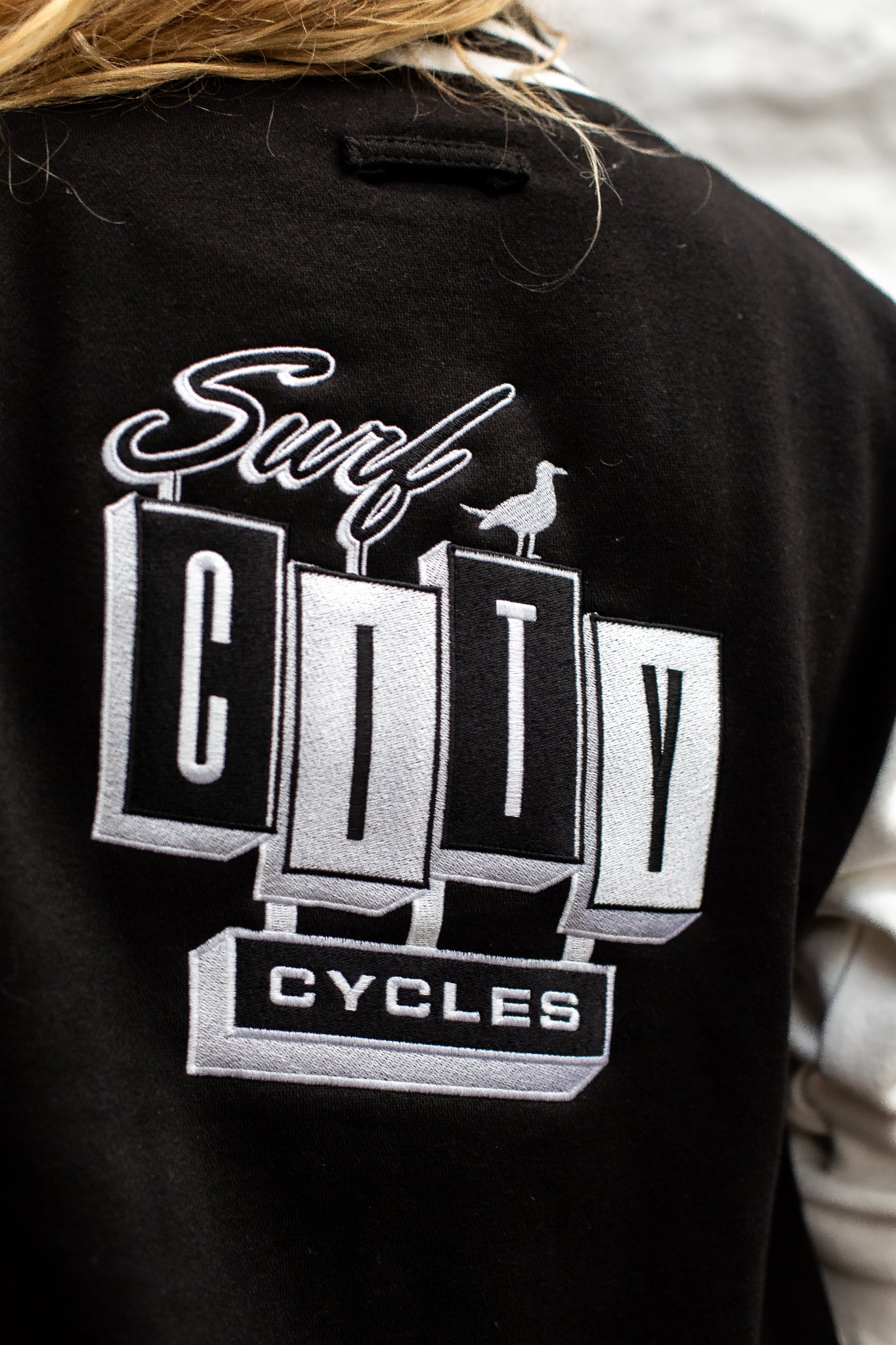 Close-up of black and cream varsity jacket by Surf City Cycles, showing stitching, cuffs, and embroidered details