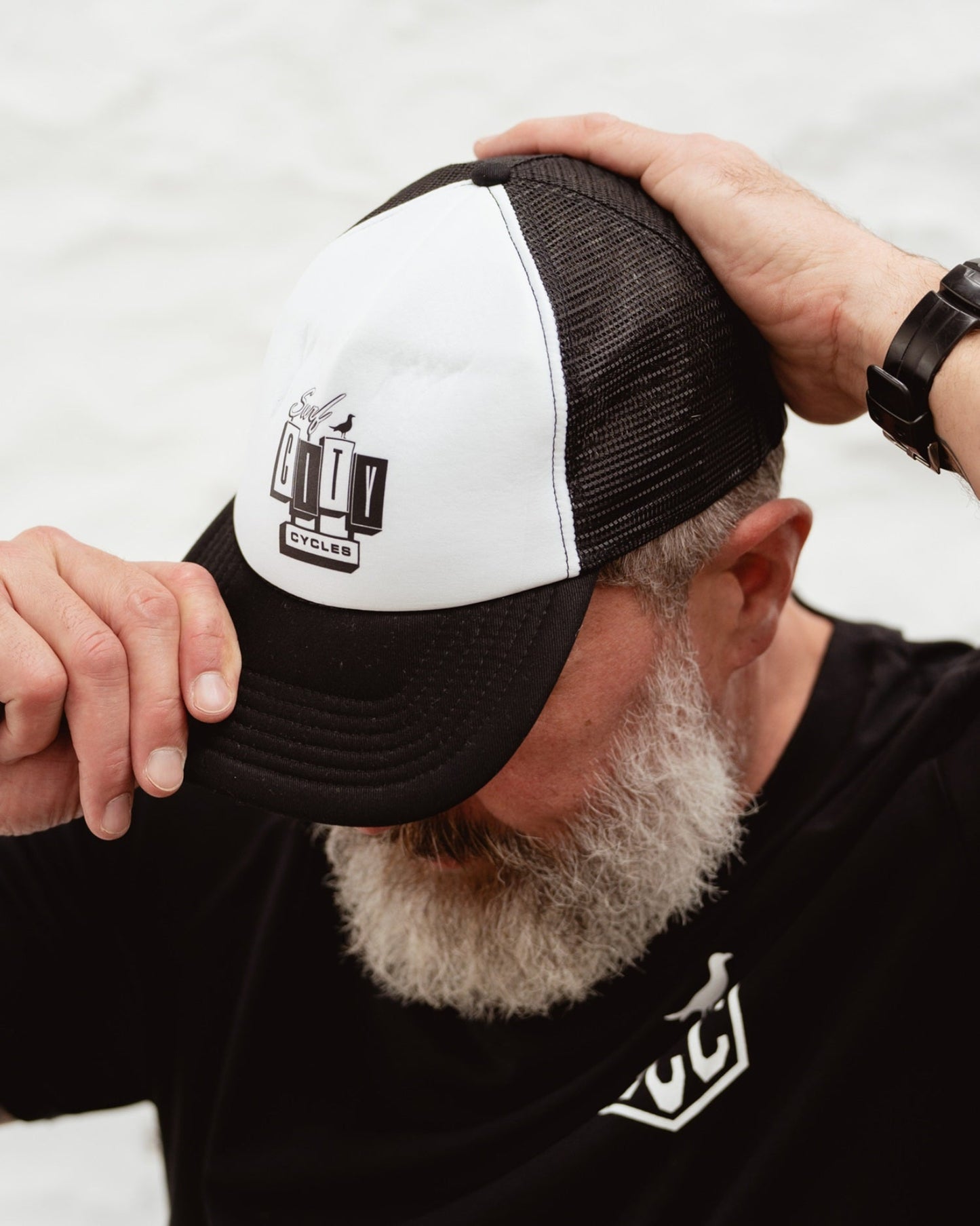 Black and white OG Logo trucker cap by Surf City Cycles worn by model outdoors, lifestyle shot, unisex
