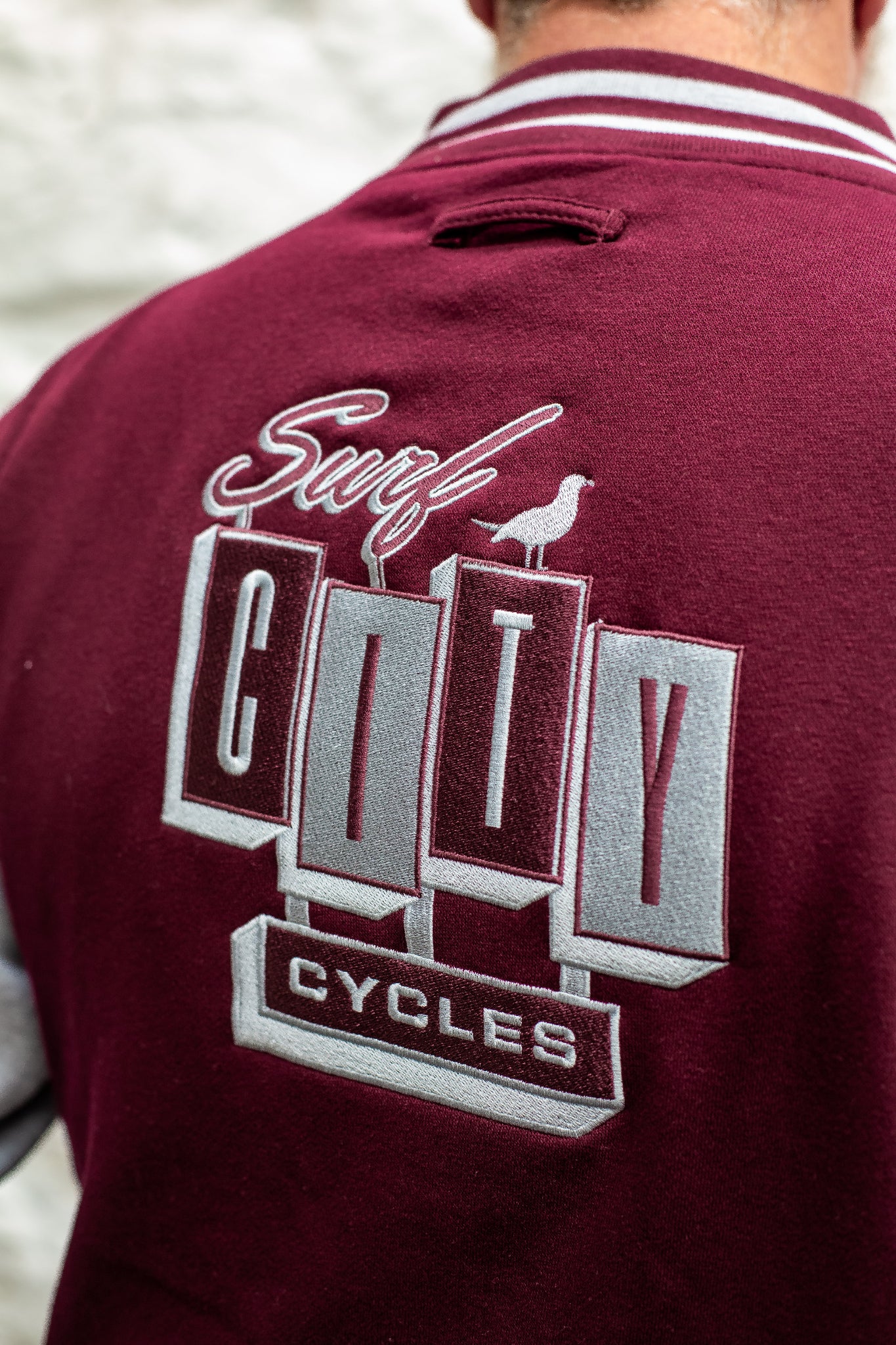 Close-up of burgundy and heather varsity jacket by Surf City Cycles, showing stitching, cuffs, and embroidered details