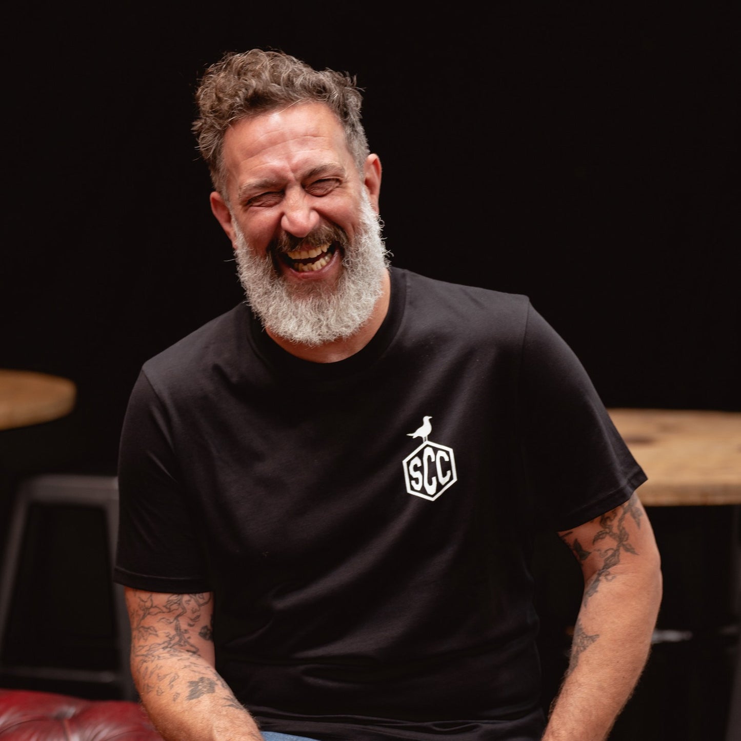 High-energy lifestyle shot of a man laughing next to a custom chopper motorcycle in a workshop.