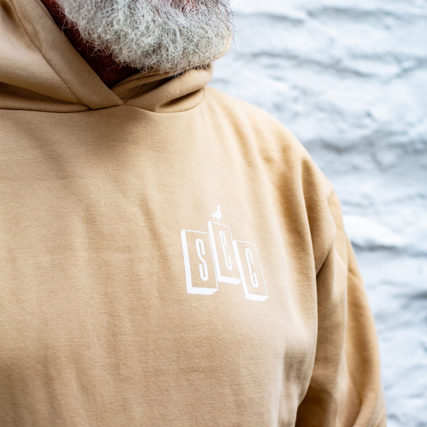 Andrew Pringle wearing the Desert Sand heavyweight Surf City Cycles OG Logo hoodie with black branding.
