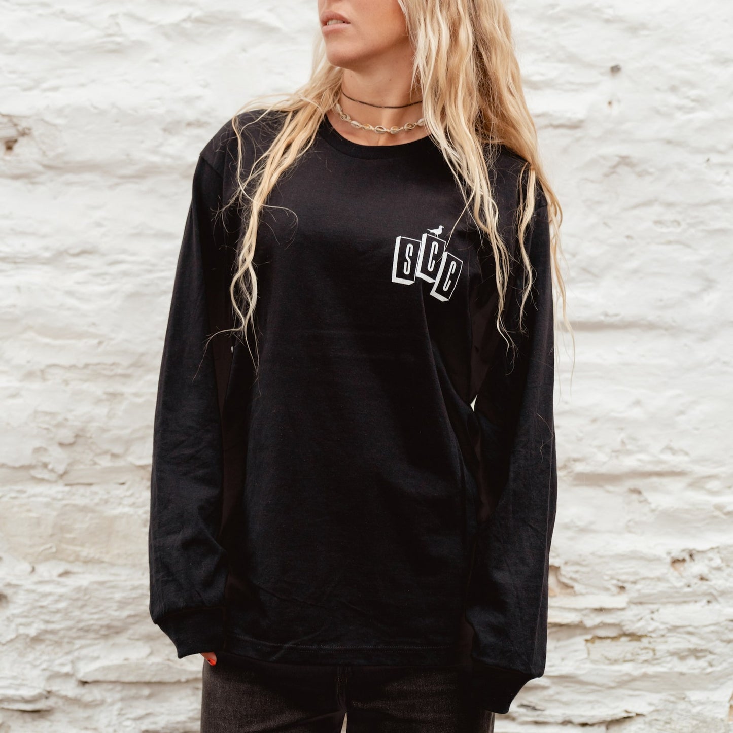 Blonde surfer girl wearing the black OG Logo long sleeve t-shirt with white Surf City Cycles branding.
