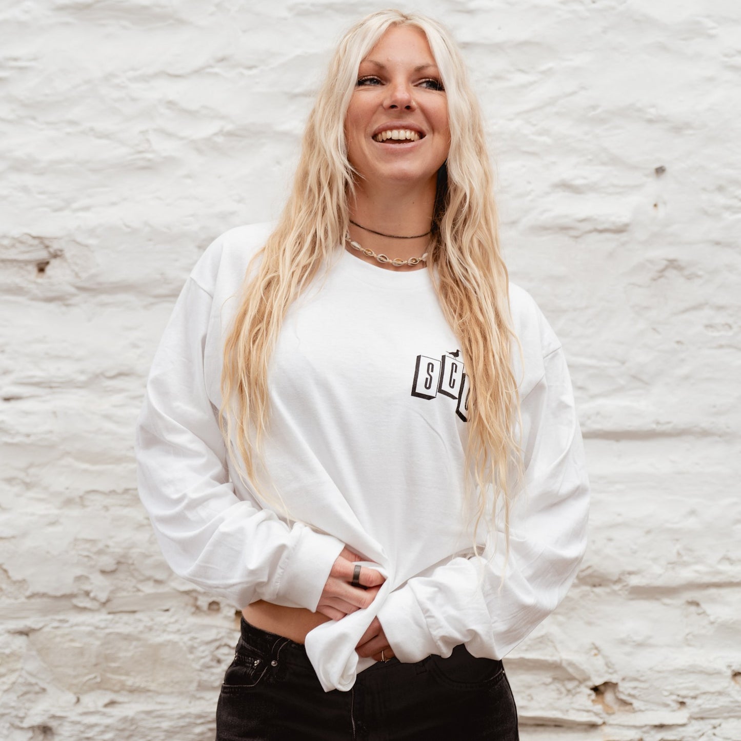 Front view of a blonde surf girl wearing the white Surf City Cycles OG Logo long sleeve t-shirt with black chest branding.