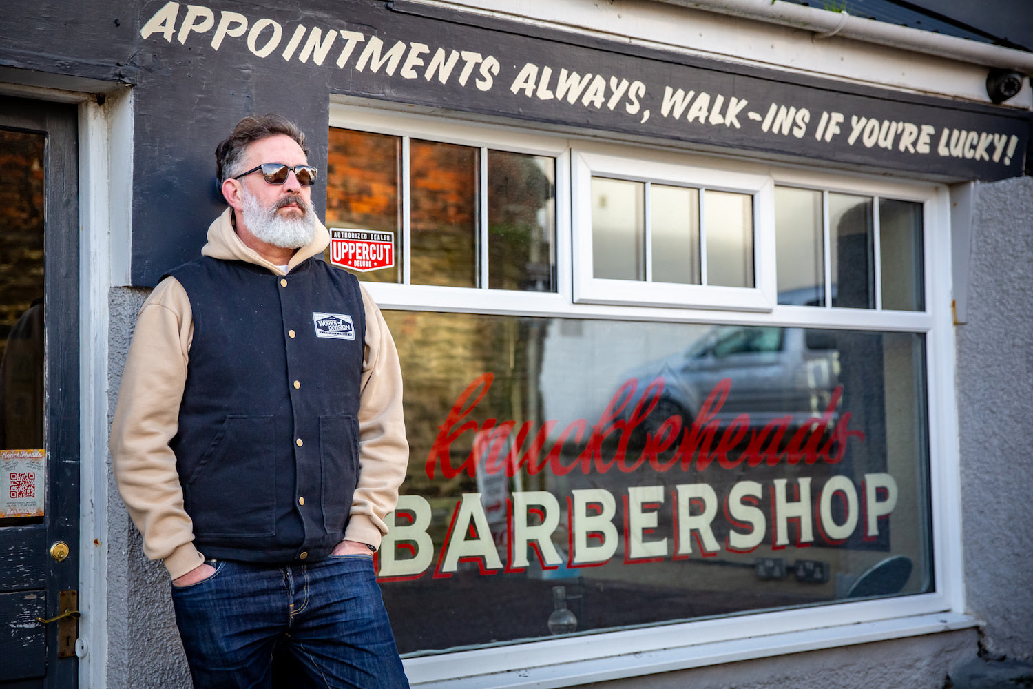 A man wearing a Works Division gilet and tan hoodie standing outside Knuckleheads Barbershop in Newquay.