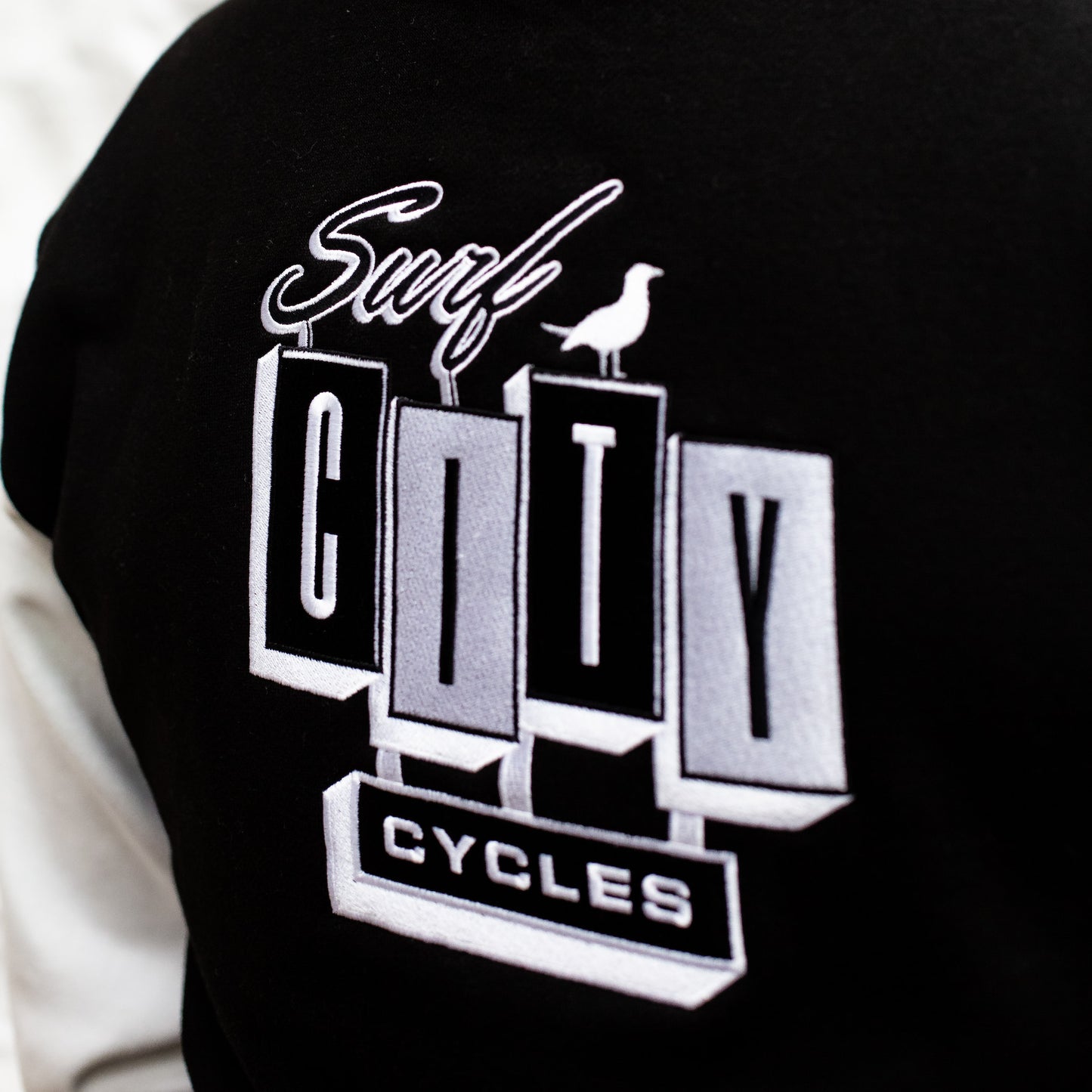Close-up of the large "Surf City Cycles" back embroidery on the black varsity jacket.