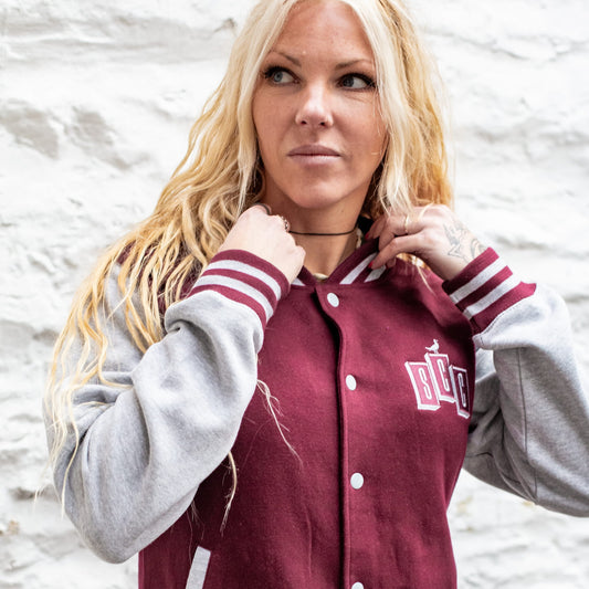 Side profile of a woman adjusting the collar of a maroon and heather grey varsity jacket.